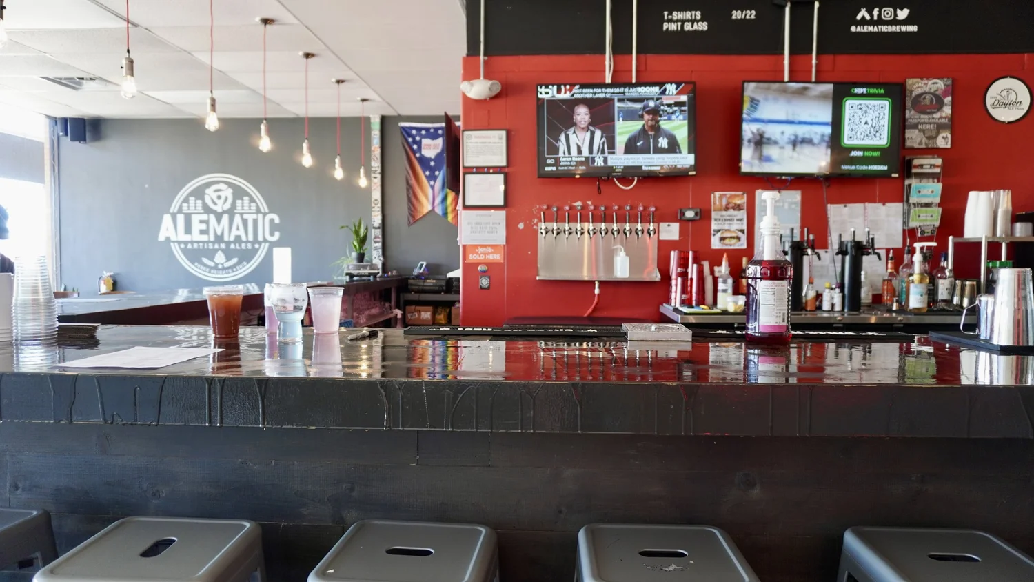 Alematic taproom bar with taps, stools, and wall logo